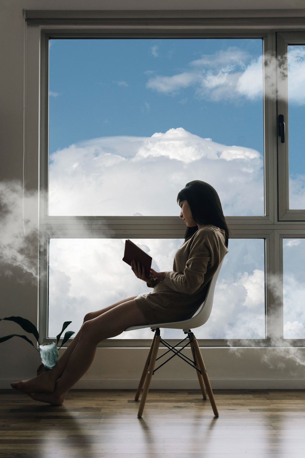 Artistic shot of woman reading indoors by a large window and clouds outside